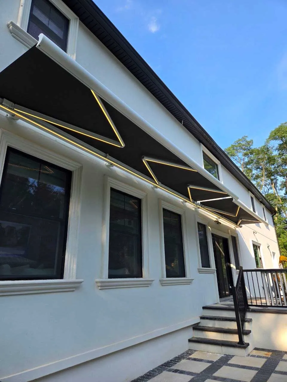 Dark retractable awning with LED lit arms extended over the back wall of a white house