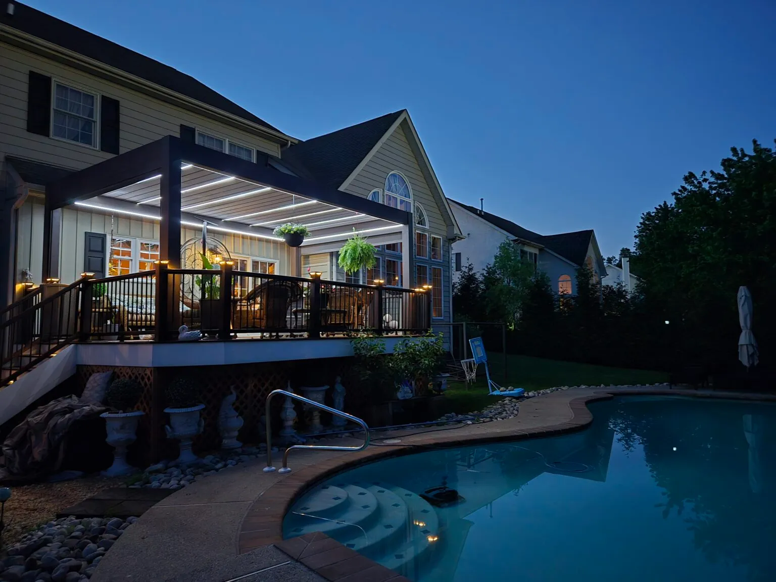 Lit pergola on a raised deck next to a pool at night